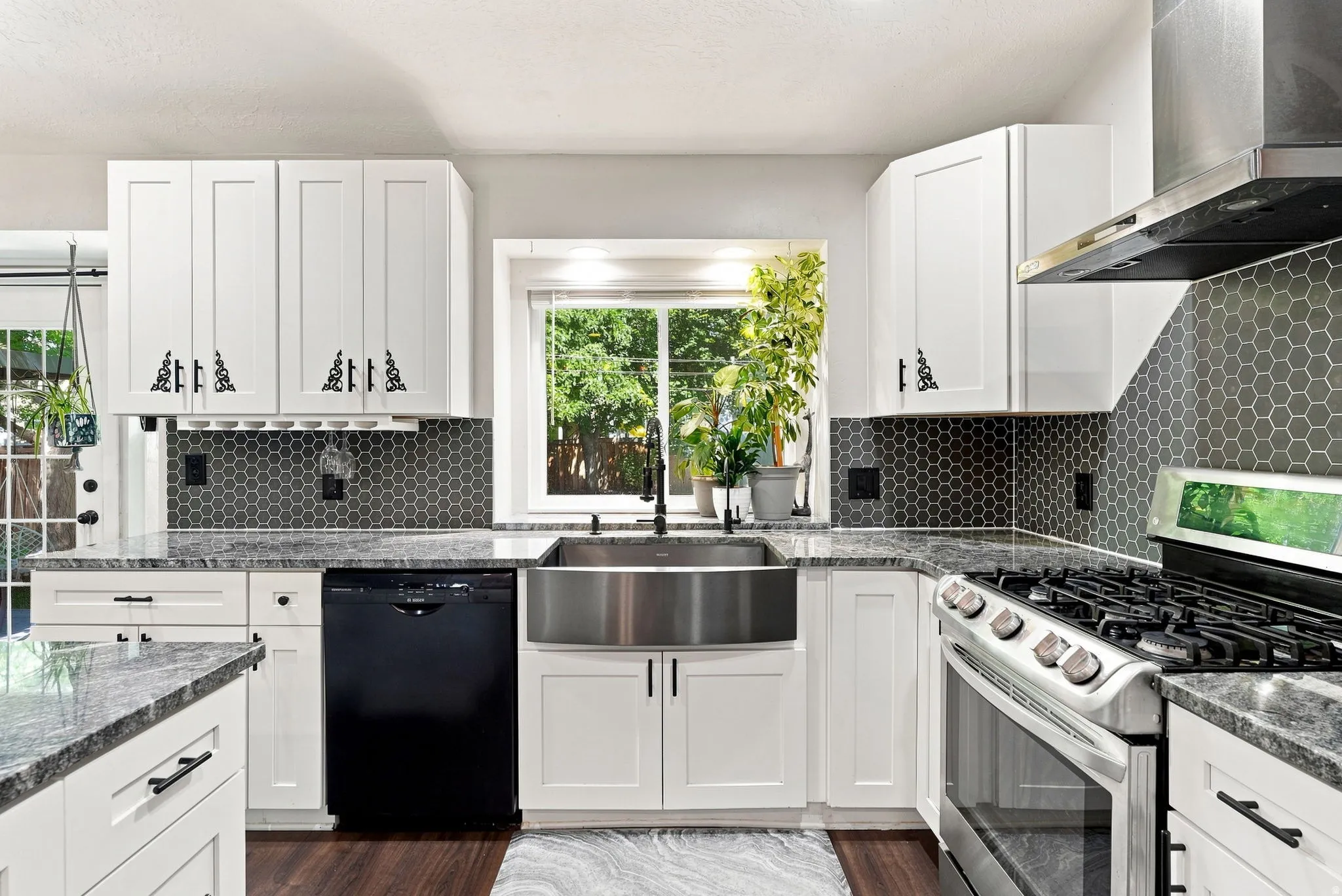 White shaker cabinetry, gray granite countertops, stainless steel farmhouse sink, hexagonal tile backsplash, and stainless steel range with hood