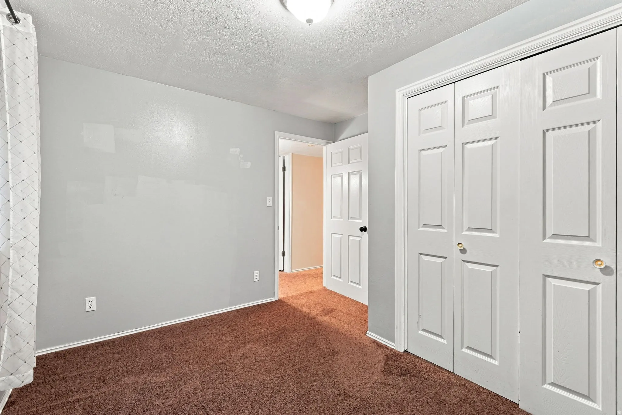 Room featuring neutral gray walls, brown carpet flooring, and white bi-fold closet doors with brass-finish hardware