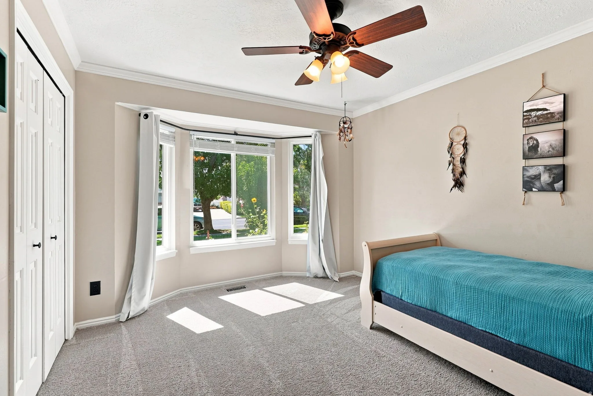 Bay window providing natural illumination, ceiling fan with integrated lighting, crown molding, and bi-fold closet doors