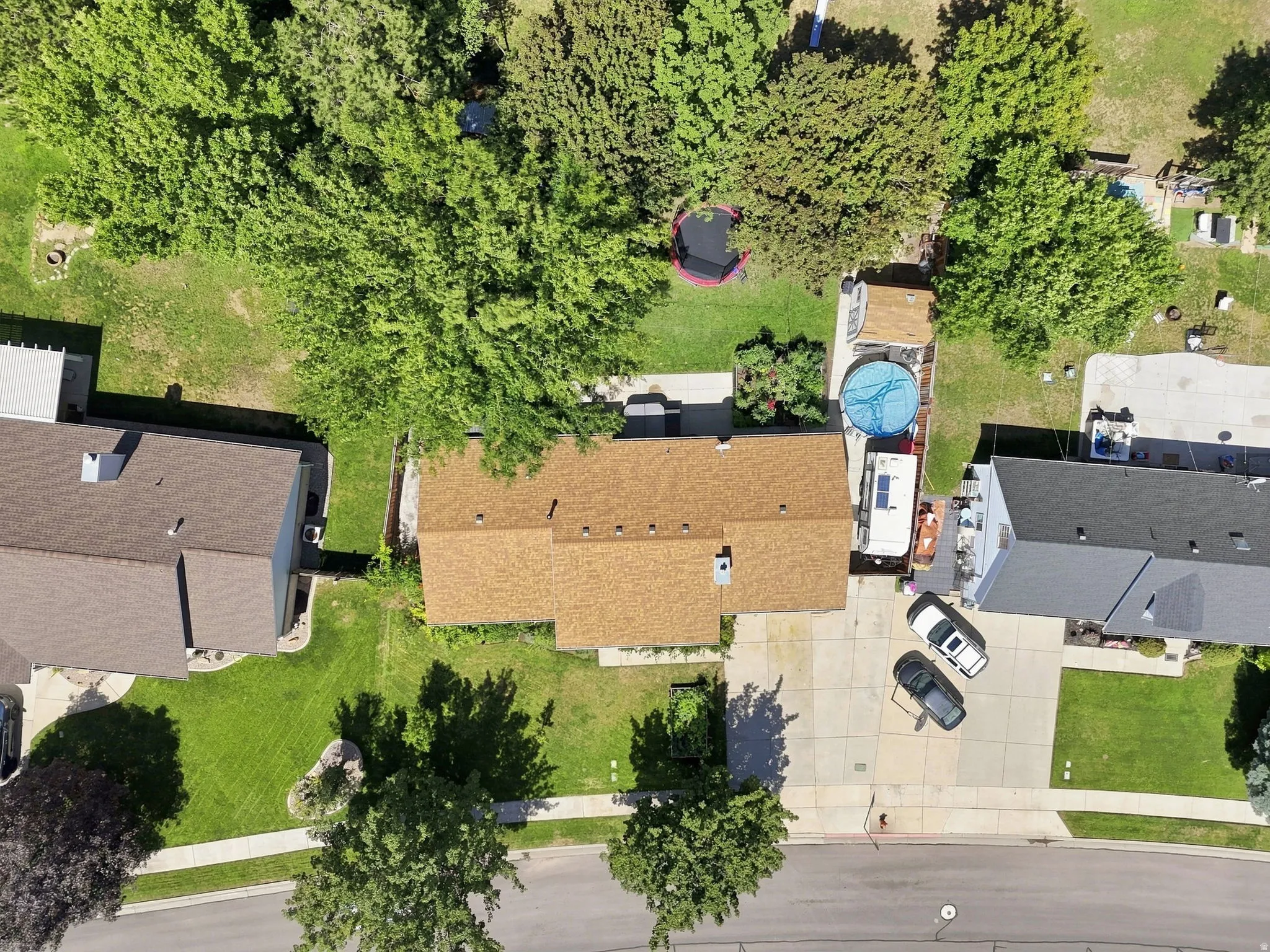 Brown shingle roof, paved driveway, mature trees, green lawn