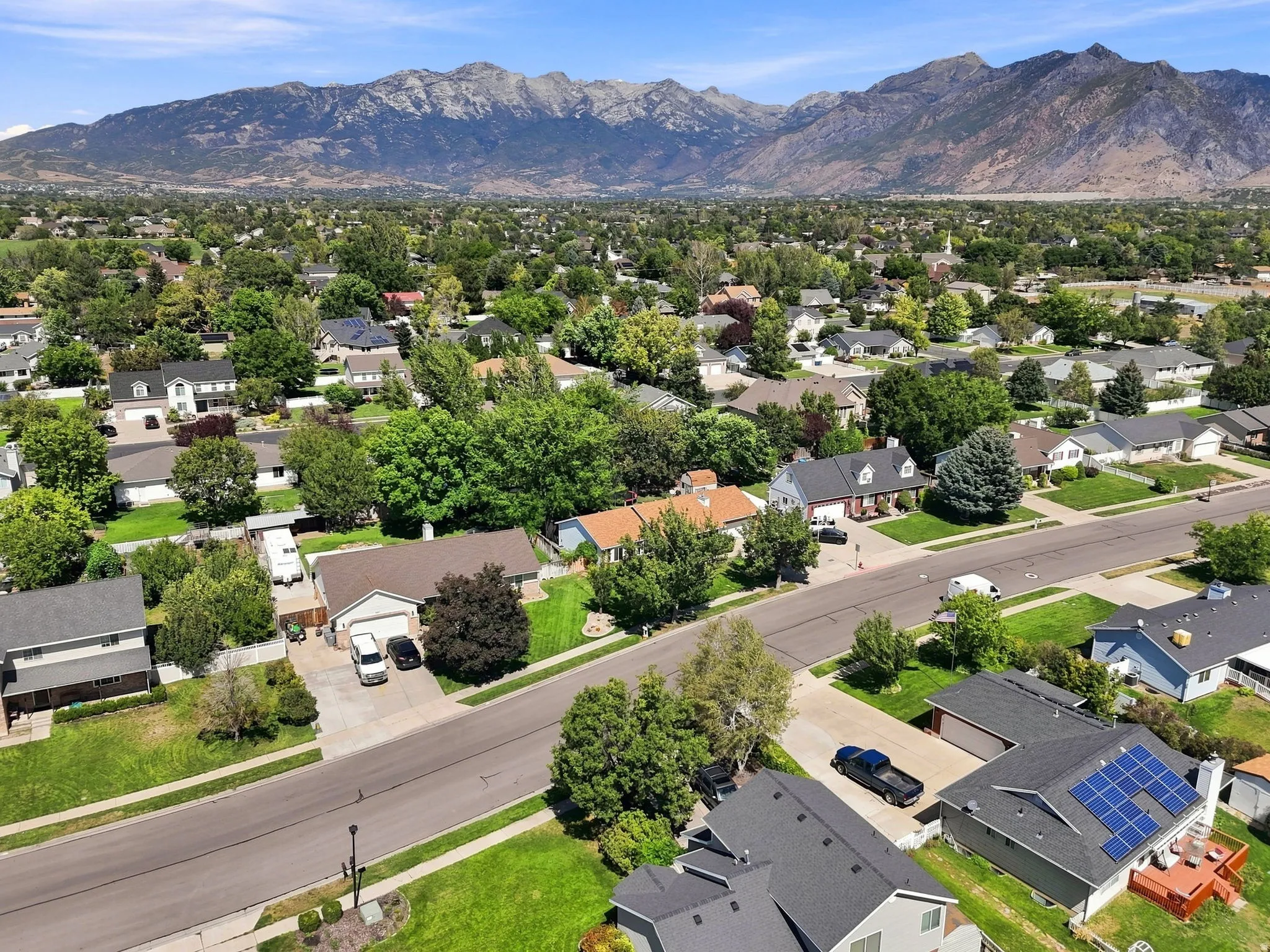 Residential neighborhood with mature trees, mountain backdrop, and multiple properties featuring solar panels