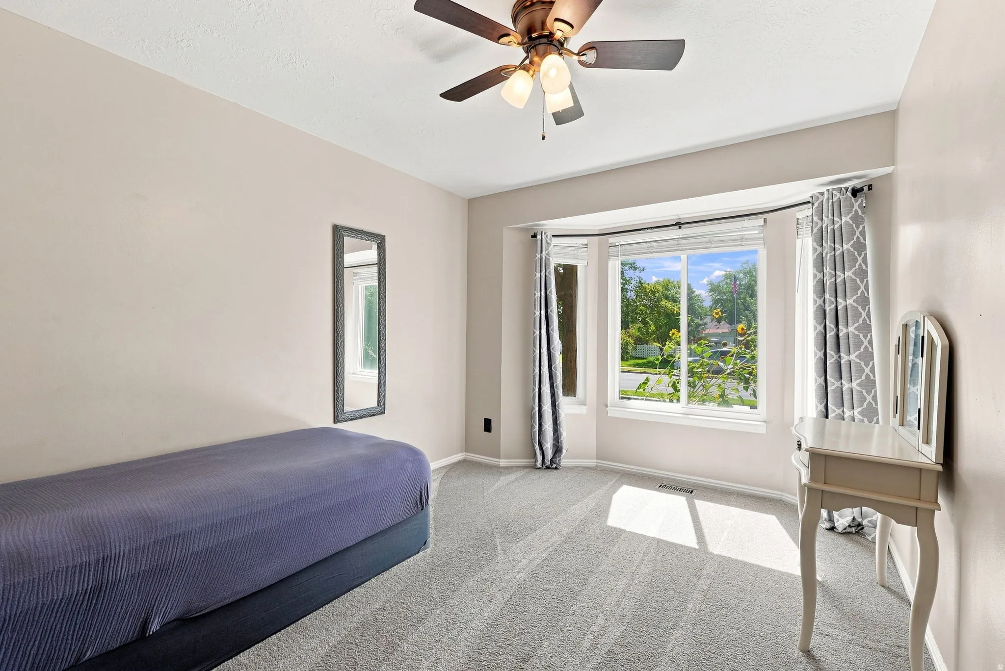 Bay window with multiple panes, ceiling fan with integrated lighting, neutral carpet flooring, and light-toned wall paint