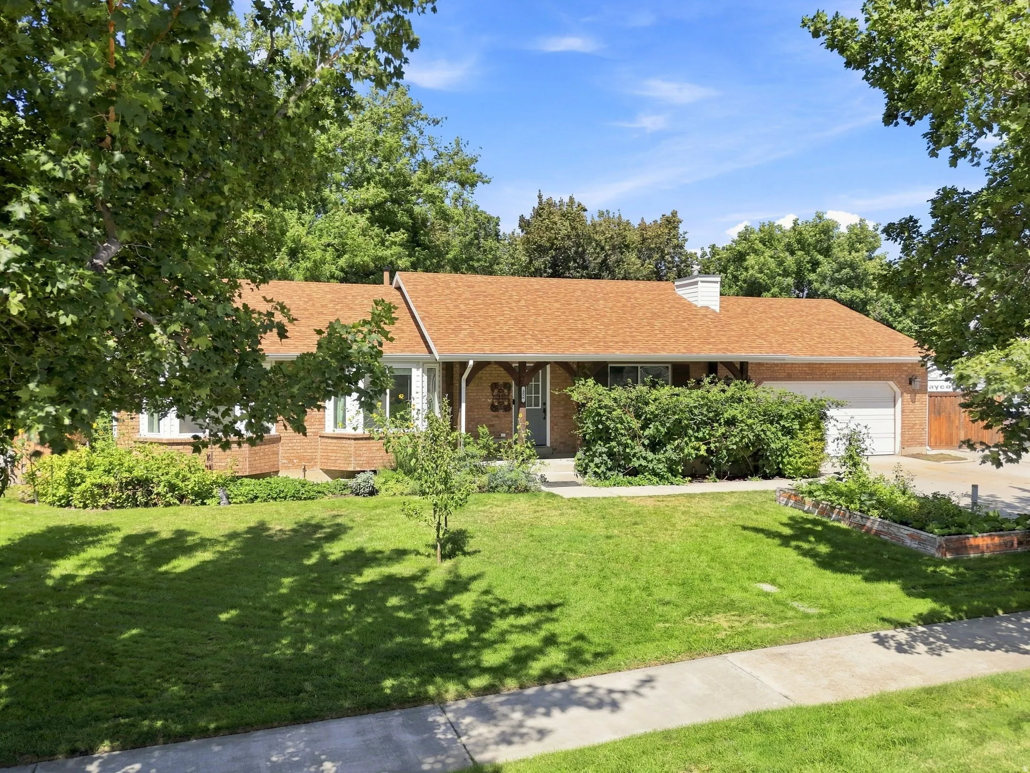 Brick exterior with an attached garage, featuring a gabled roof and mature front landscaping