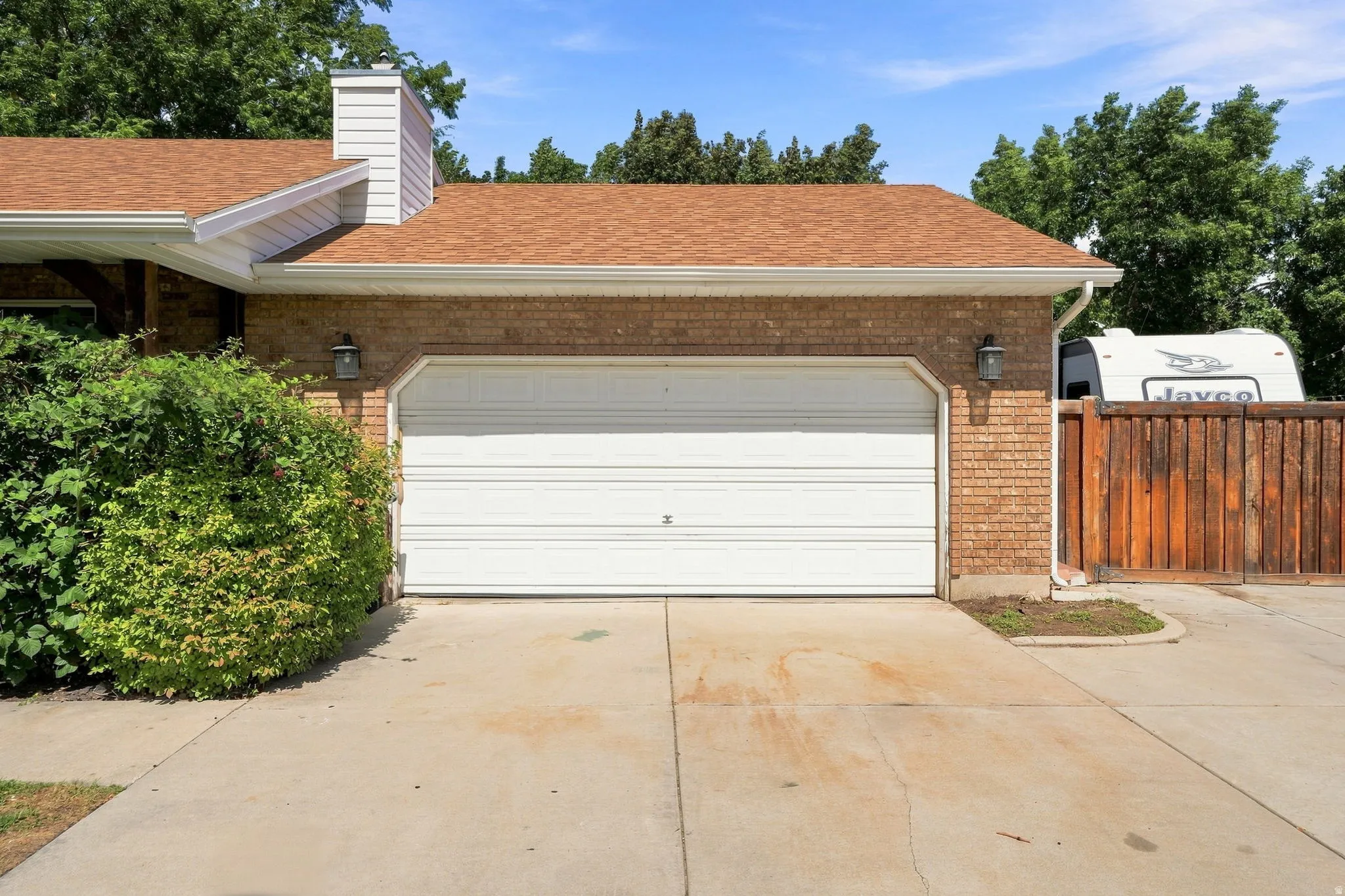 Brick exterior featuring a two-car garage, concrete driveway, and wood fencing