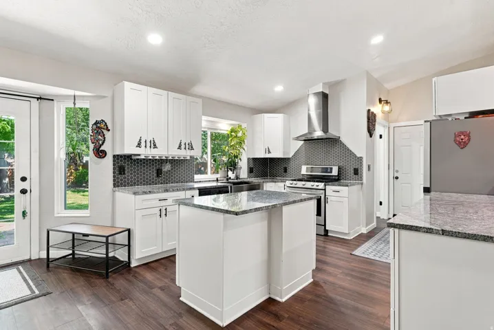Kitchen featuring white shaker cabinetry, stainless steel appliances, speckled countertops, a hex-tile backsplash, and wood-finish flooring