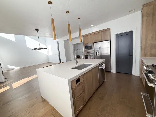 Kitchen featuring a large central island with an integrated sink, wood-finish flooring, stainless steel appliances, and wood-finish cabinetry