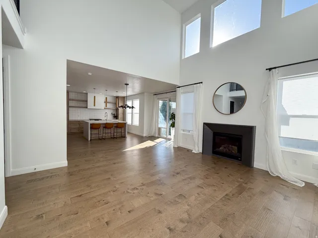 Open-concept living space featuring wood-finish flooring, a contemporary fireplace, and high ceilings with multiple windows