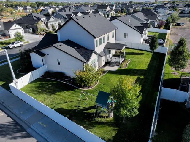 Fenced backyard with manicured lawn, mature trees, and covered patio