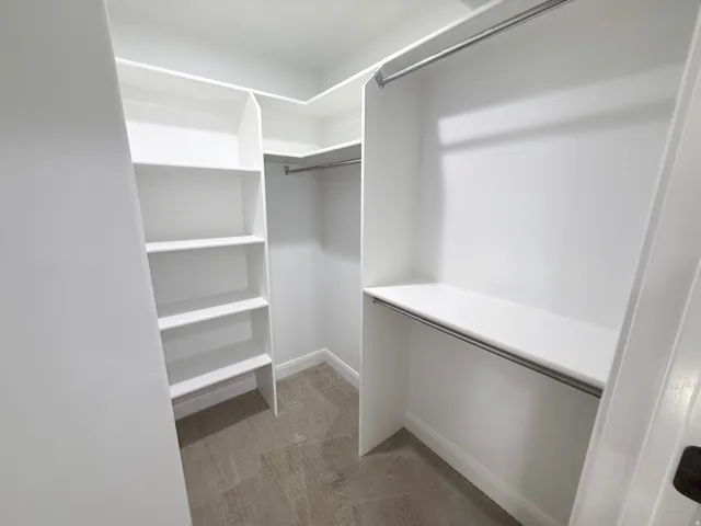 White built-in shelving, white walls, white trim, metal hanging rods, and carpet flooring