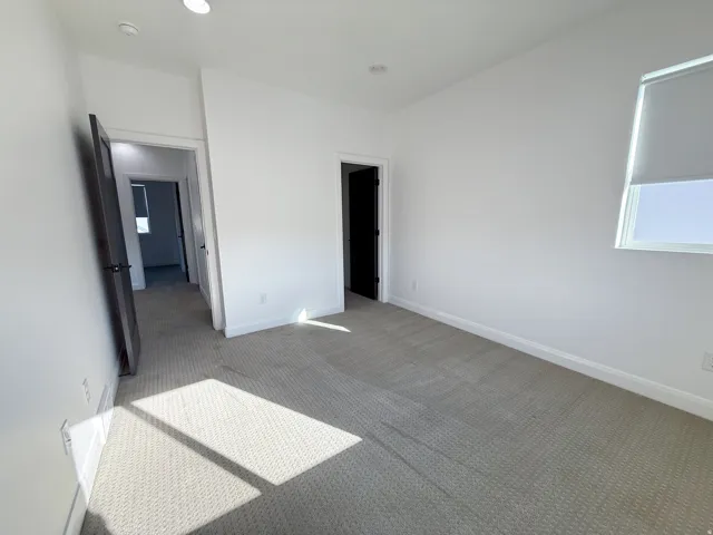 Recessed lighting, light-colored carpeting, white walls, and a window with a roller shade