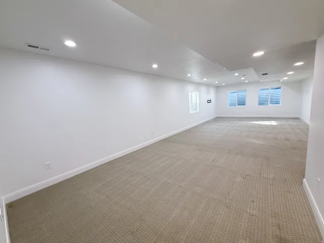 Spacious room featuring neutral carpet, white walls, multiple recessed lights, and horizontal blinds on multiple windows