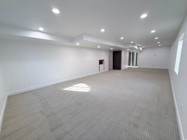 Recessed lighting, light-toned carpeting, white painted walls, and dark interior doors