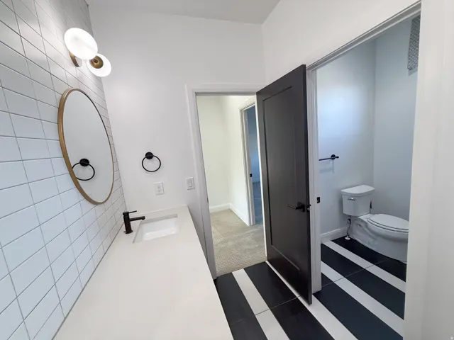 Vanity with integrated sink, rectangular white tile backsplash, gold-framed oval mirror, and matte black faucet