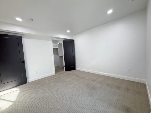 Recessed ceiling lighting, white walls, dark paneled doors, light carpet, and built-in closet shelving