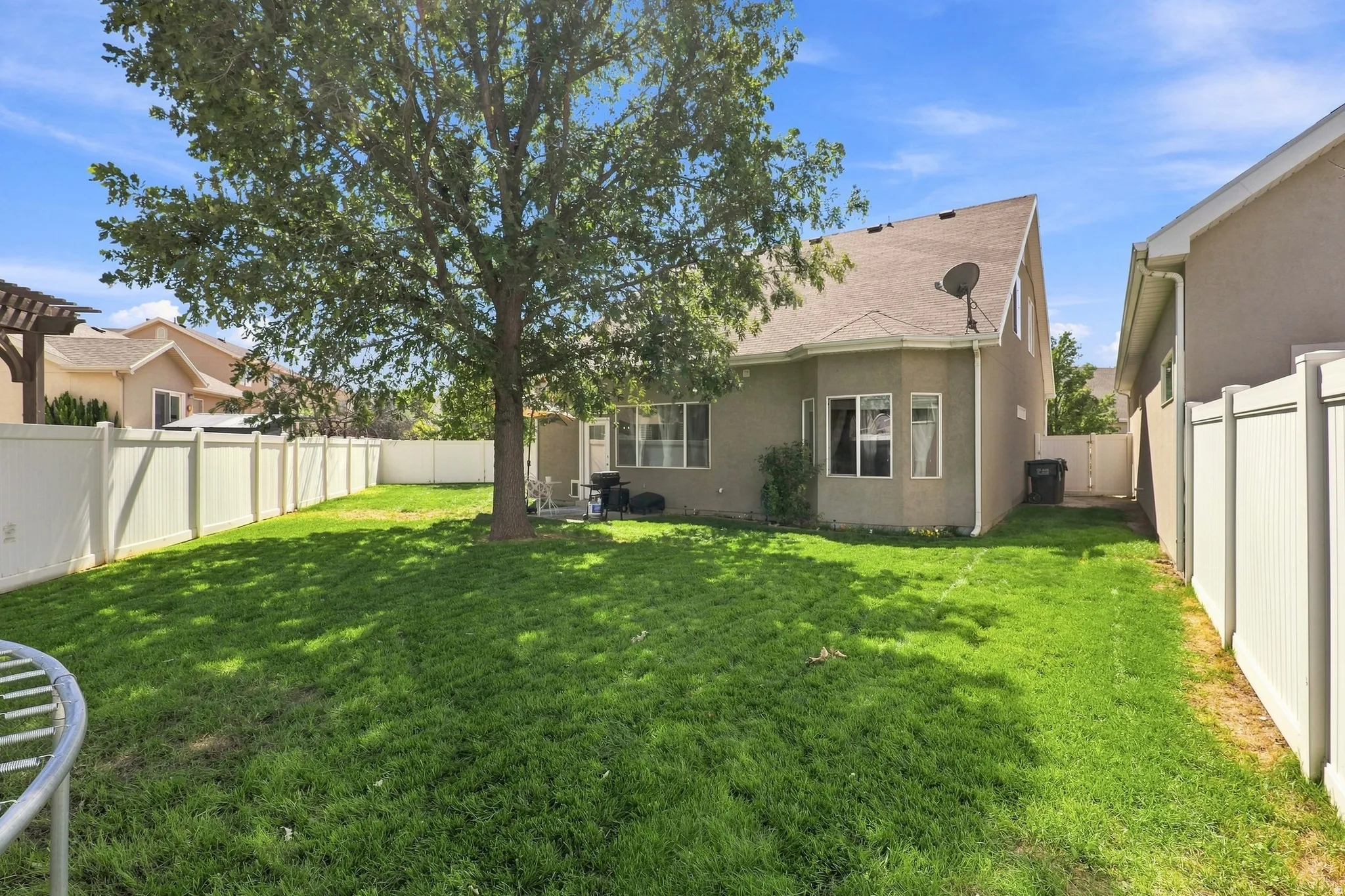 Expansive grassy yard with a mature shade tree, full privacy fencing, and a concrete patio area