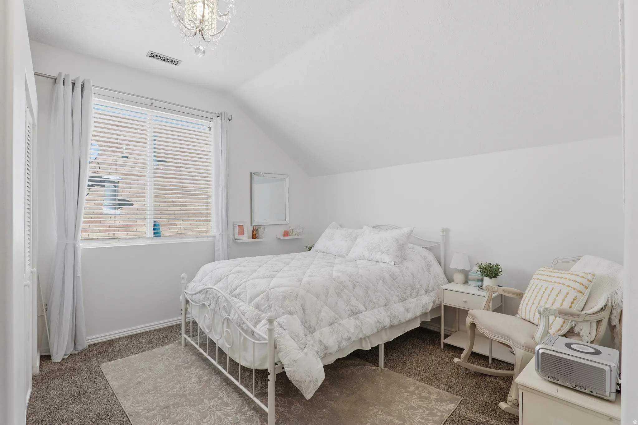 White-painted interior with sloped ceiling, carpeted flooring, and a crystal chandelier