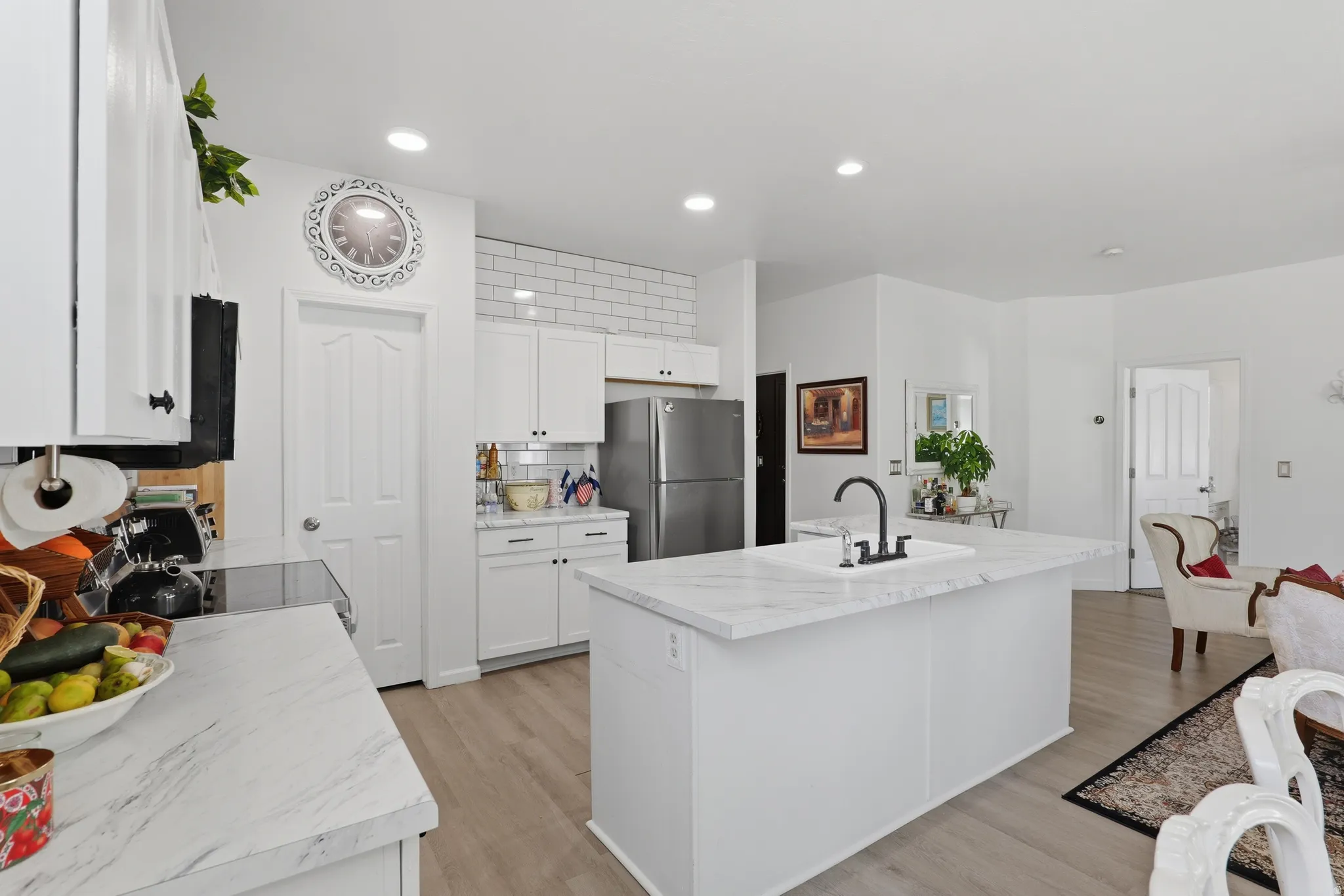Bright kitchen with white cabinetry, wood-finish flooring, white countertops, and a subway tile backsplash