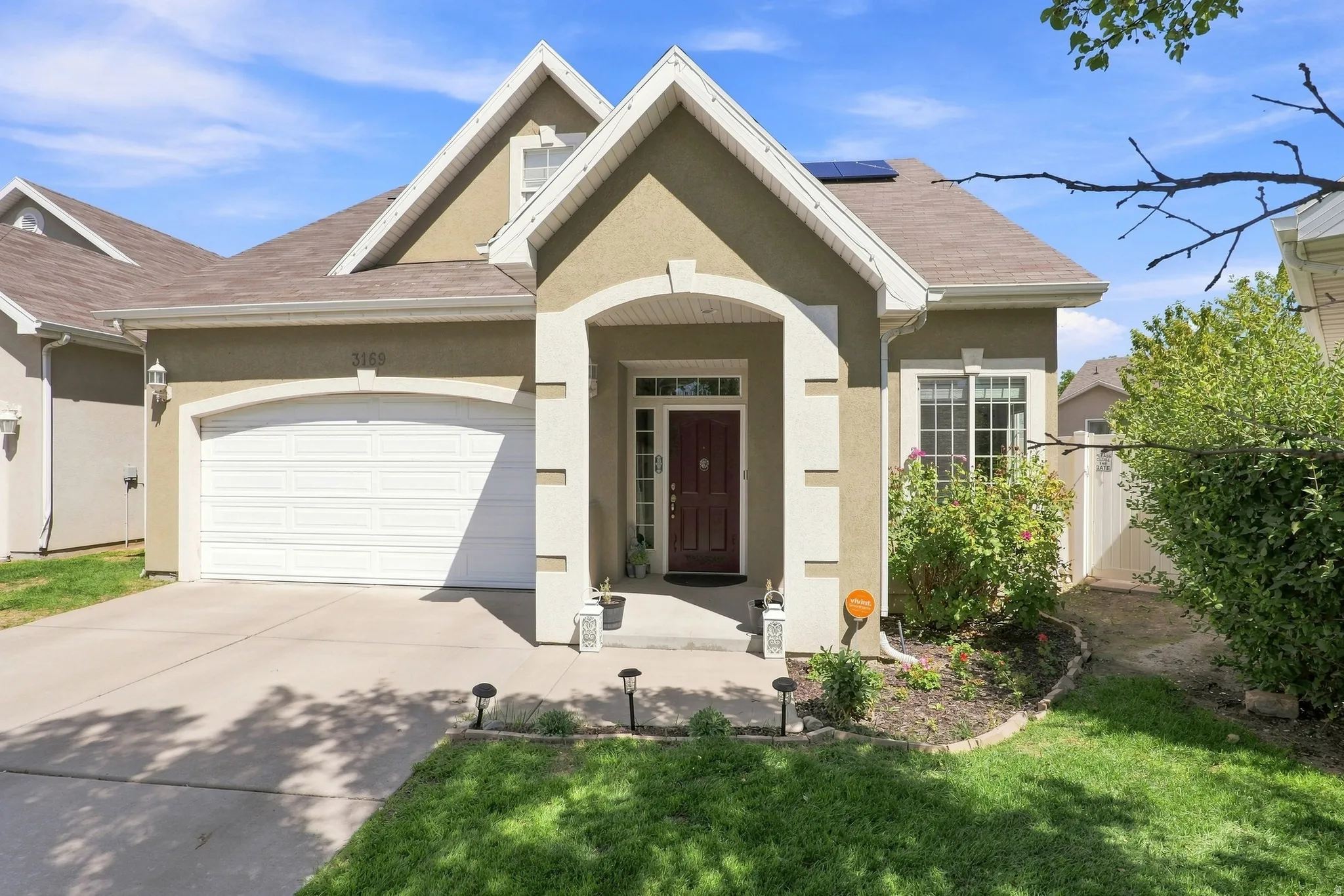 Stucco exterior with gabled roof lines, attached garage, concrete driveway, and established front landscaping