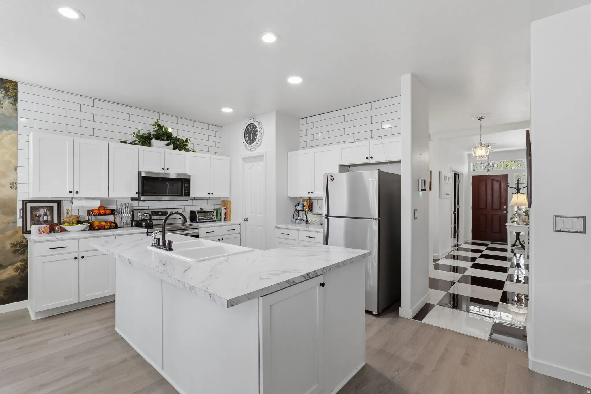 Kitchen featuring white shaker cabinetry, subway tile backsplash, white countertop island, stainless steel appliances, and wood-finish flooring