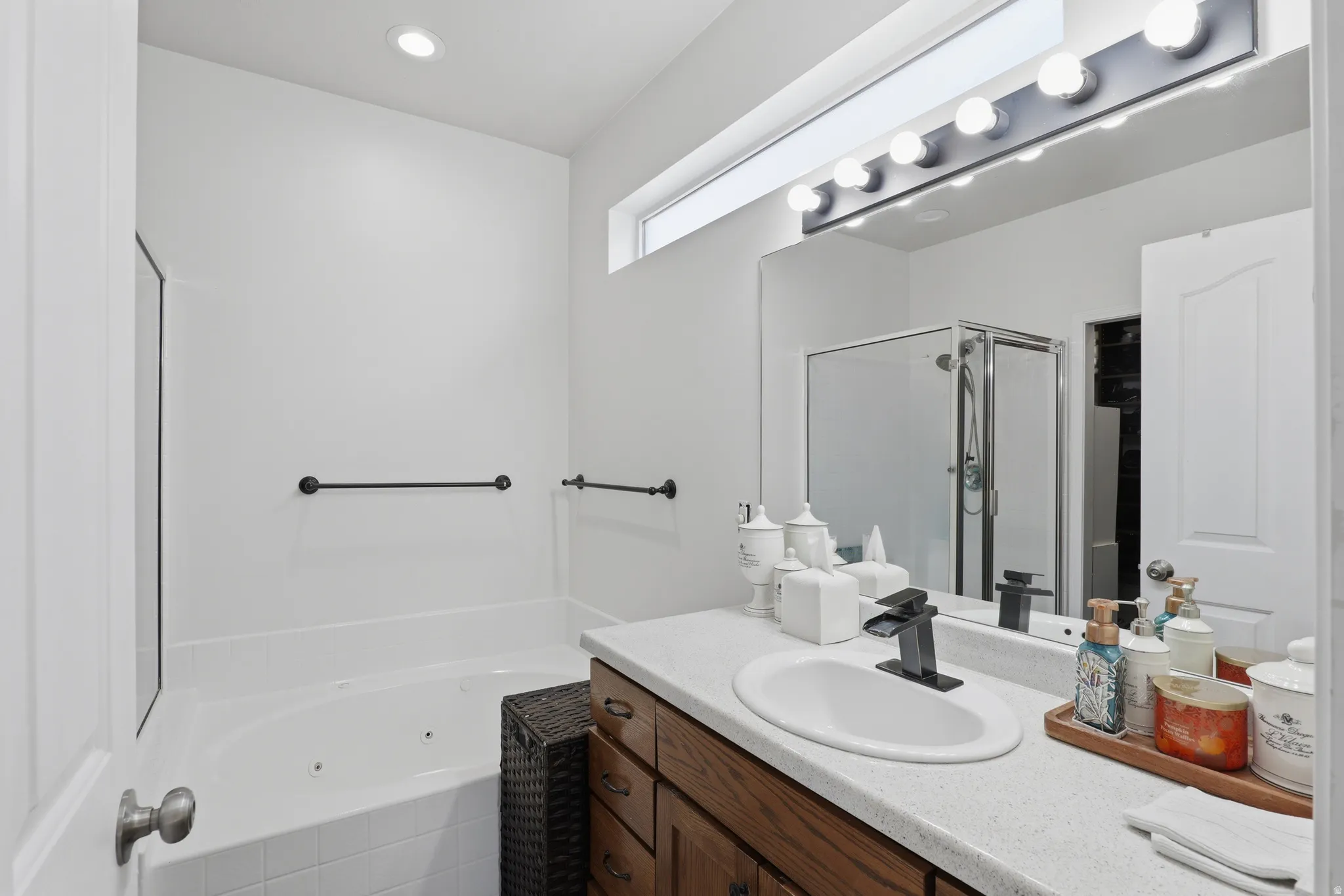 Recessed ceiling lighting, jetted tub, wood-finish vanity with ample storage, integrated white sink, and large vanity mirror with overhead lighting