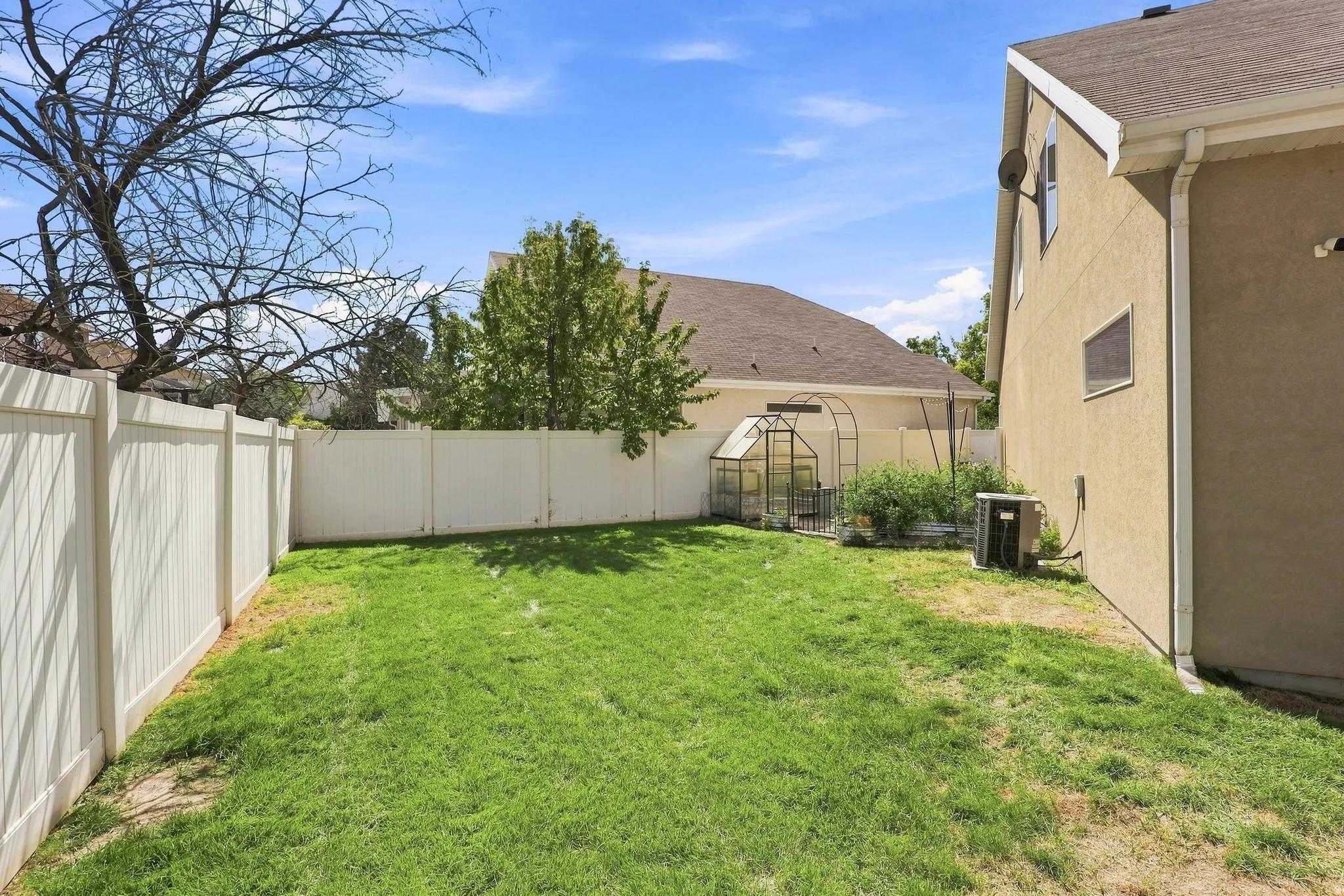 Expansive backyard featuring a green lawn, full perimeter fencing, and a built-in greenhouse structure