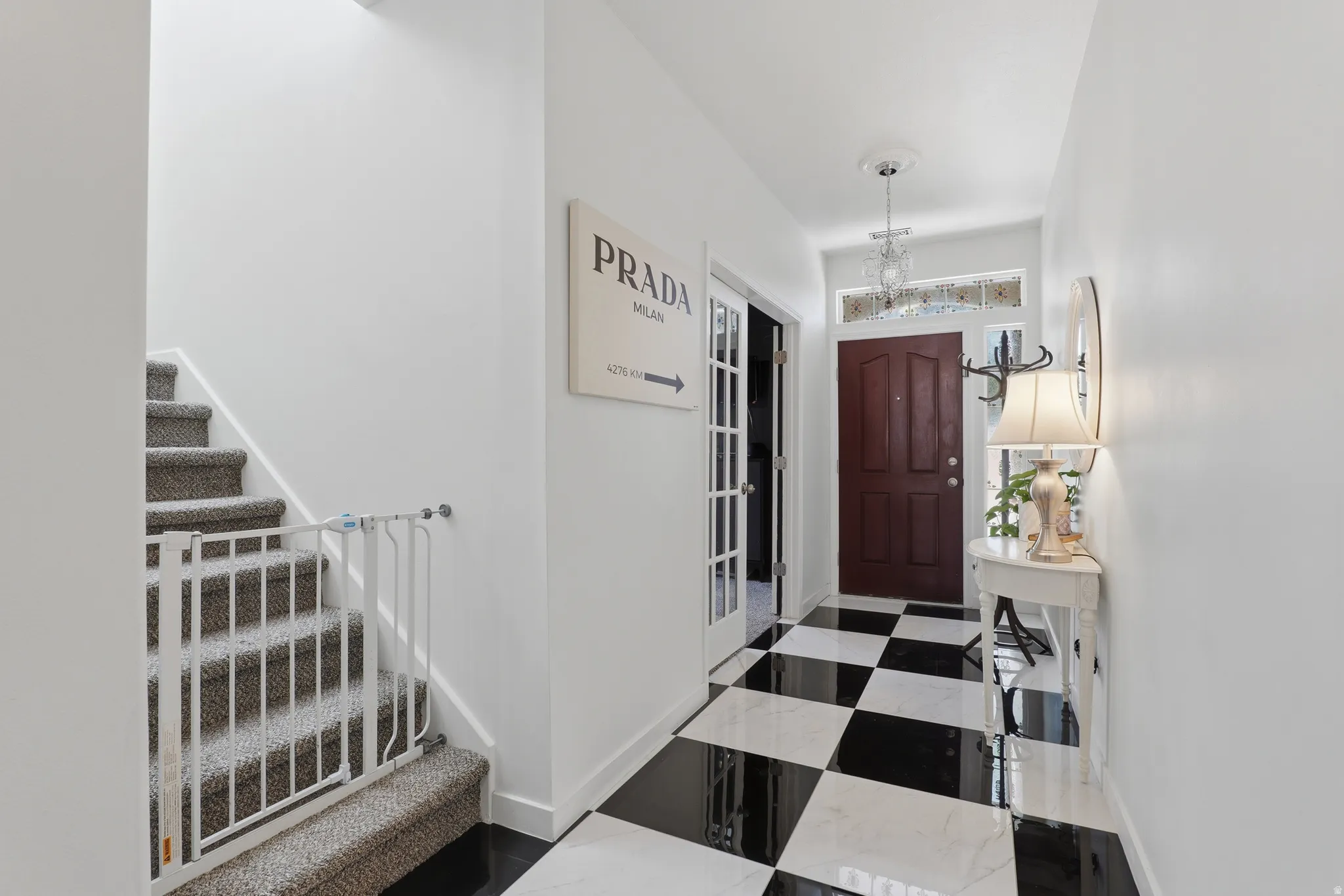 Black and white checkered tile flooring, wood-paneled door, transom window, and a crystal chandelier