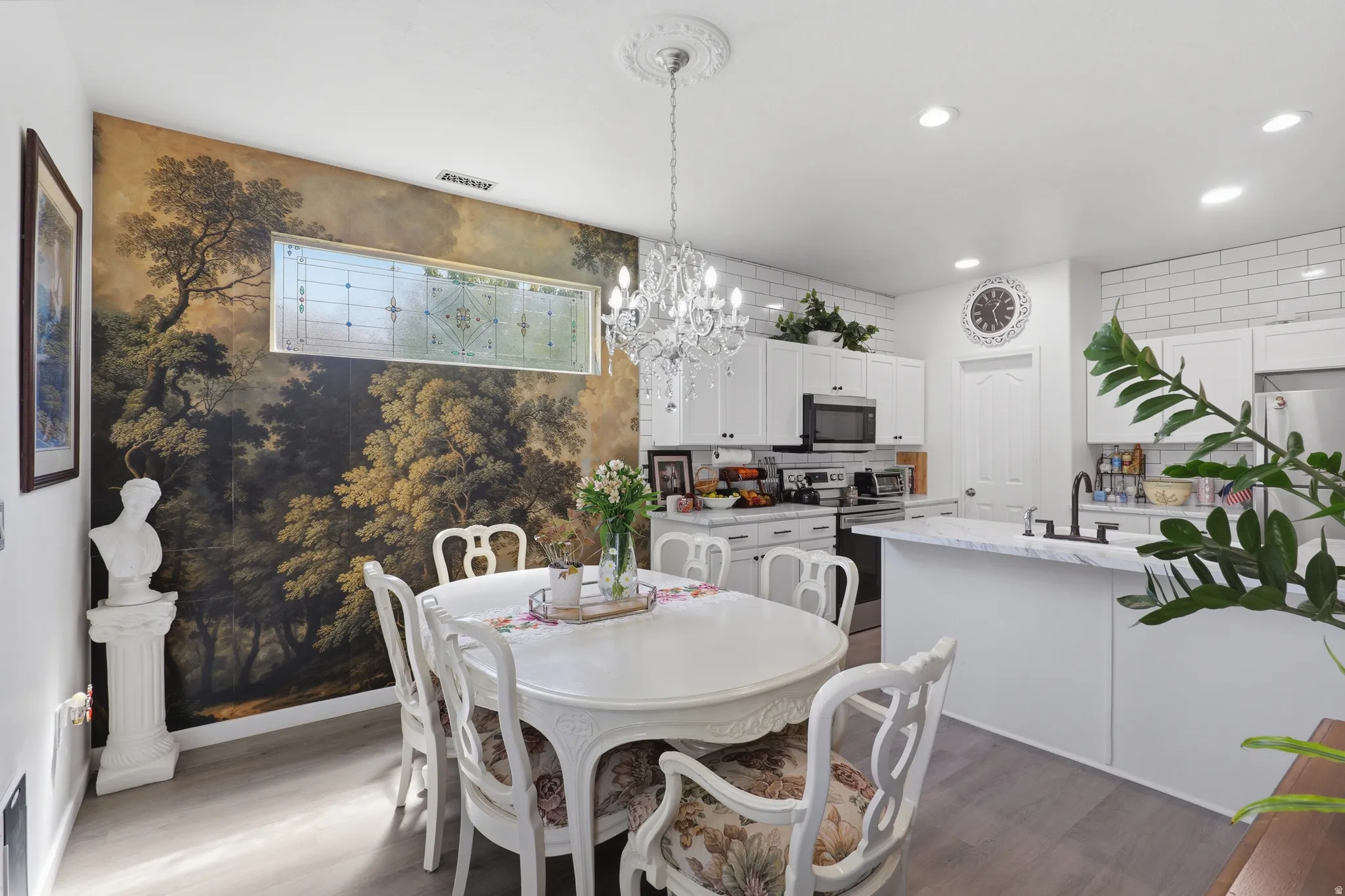 Open-concept living space with wood-finish flooring, a decorative feature wall, and a crystal chandelier