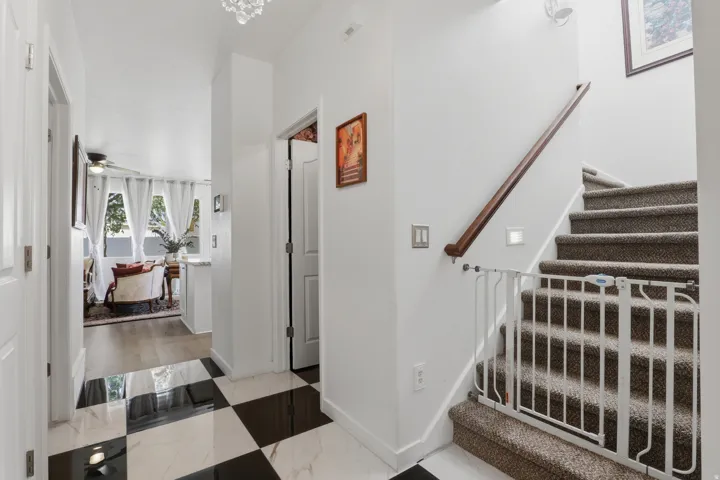 Black and white checkered tile flooring, carpeted staircase with wood handrail, and white walls