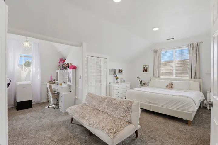 Carpeted flooring, vaulted ceiling, recessed lighting, window with blinds, and a built-in closet with louvered doors
