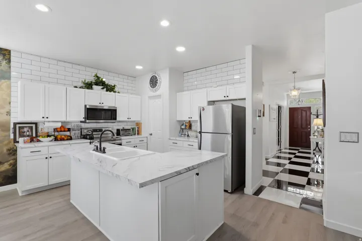 Kitchen featuring white shaker cabinetry, subway tile backsplash, white countertop island, stainless steel appliances, and wood-finish flooring