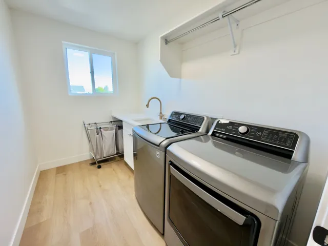 Laundry room featuring wood-finish flooring, a utility sink with a gooseneck faucet, and an upper storage shelf with a hanging rod