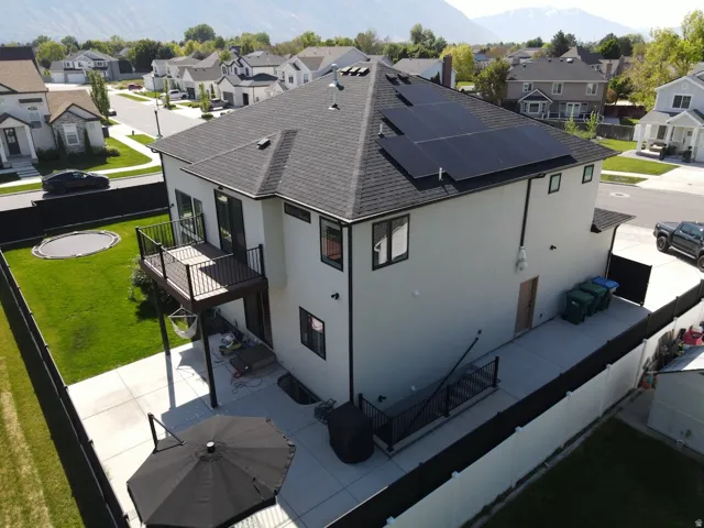 Rear exterior featuring solar panels, a second-story deck with dark railings, a concrete patio, and a manicured lawn