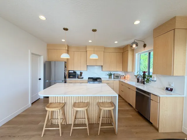 Kitchen featuring a spacious island with wood slat detailing, light wood-finish cabinetry, integrated stainless steel appliances, and wood-finish flooring
