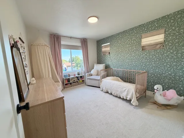 Light-colored carpeting, a window with drapery, and a contrasting accent wall with botanical-patterned wallpaper
