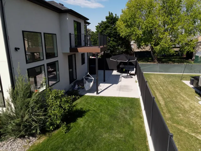 White stucco exterior with black-framed windows, a second-story balcony, a ground-level patio, and a manicured lawn