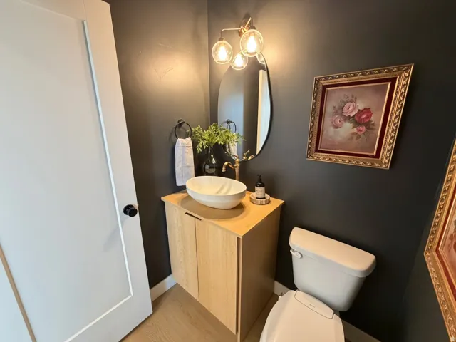 Pedestal vanity with wood-finish cabinetry, vessel sink, and an oval mirror with an attached three-bulb vanity light