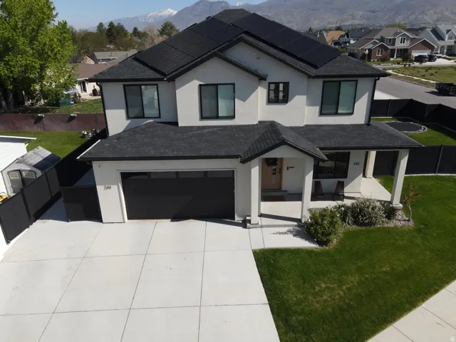 Two-story residence featuring a light-colored stucco exterior, dark-framed windows, and a dark shingled roof with integrated solar panels