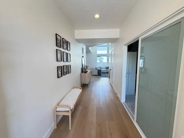 Light wood-finish flooring, recessed lighting, white walls, and a sliding glass door with integrated blinds