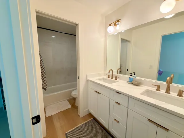 Dual vanity with white shaker-style cabinetry, white countertops, and gold-finish fixtures