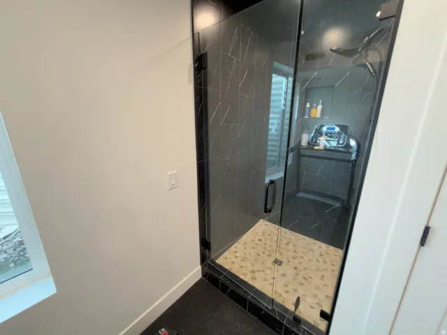 Enclosed shower with black-framed glass, stone-tiled floor, and dark veined wall tile