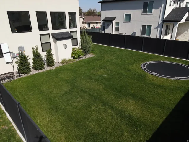 Manicured lawn with mature landscaping, contemporary black fencing, and a modern stucco exterior featuring large dark-framed windows
