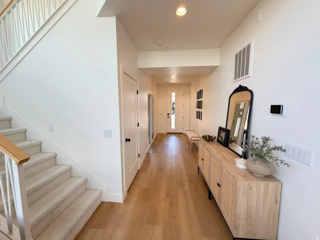 Wood-finish flooring, staircase with carpeted treads and wood handrail, white walls, and a modern front entry door with vertical glass inserts