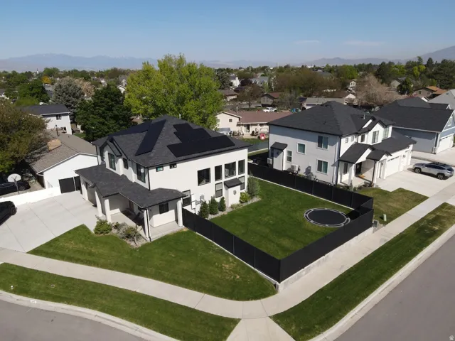 Contemporary residence featuring a dark shingle roof, solar panels, a fenced backyard, and an attached two-car garage