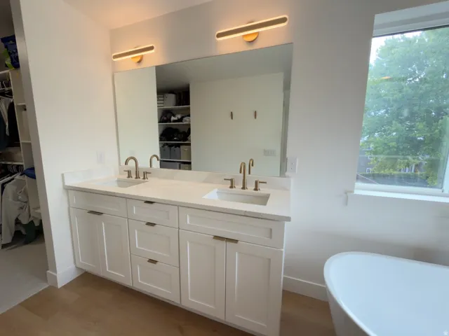 Dual vanity with white cabinetry and brushed brass hardware, complemented by a large mirror and modern light fixtures