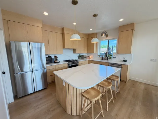 Light wood-finish cabinetry, stainless steel appliances, solid surface countertops, a center island with slatted wood detailing, and wood-finish flooring