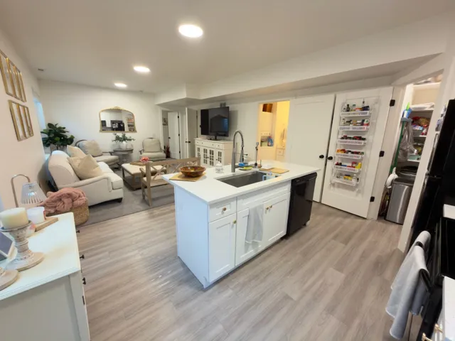 Central kitchen island with an integrated sink, white cabinetry, and a black dishwasher
