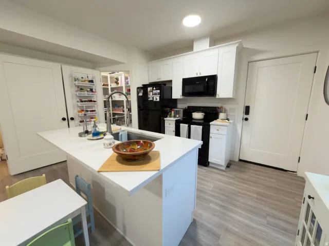 Kitchen featuring a central island with an undermount sink, white cabinetry, black appliances, and wood-finish flooring