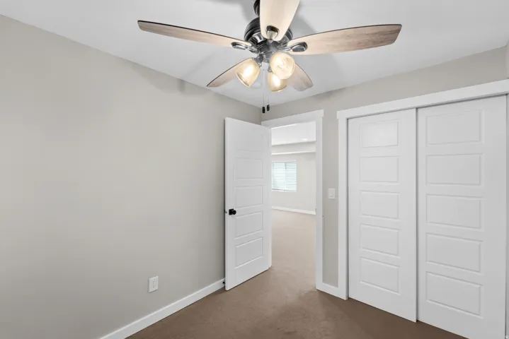 Ceiling fan with light kit, flat panel interior doors, sliding closet doors, and carpet flooring
