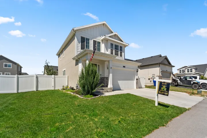 Two-story property featuring a front porch with columns, a two-car garage, and a white privacy fence
