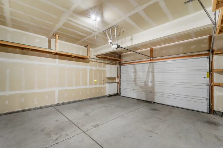 Concrete flooring, built-in overhead shelving, automatic garage door opener, built-in cabinetry, and overhead lighting